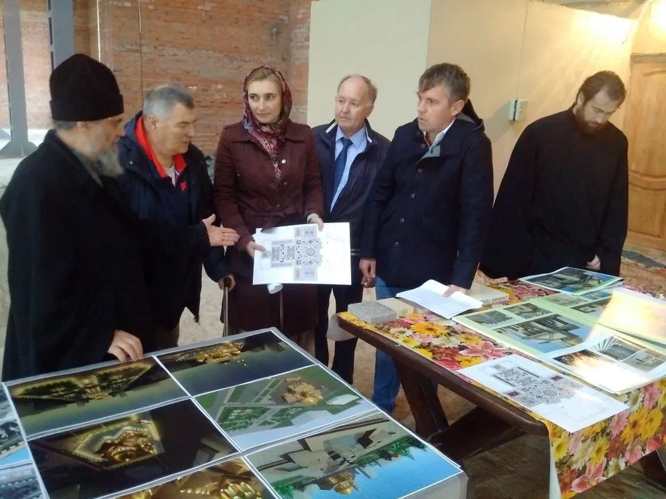 Митрополит и представители власти рассматривают архитектурные чертежи собора внутри неотделанного кирпичного зала